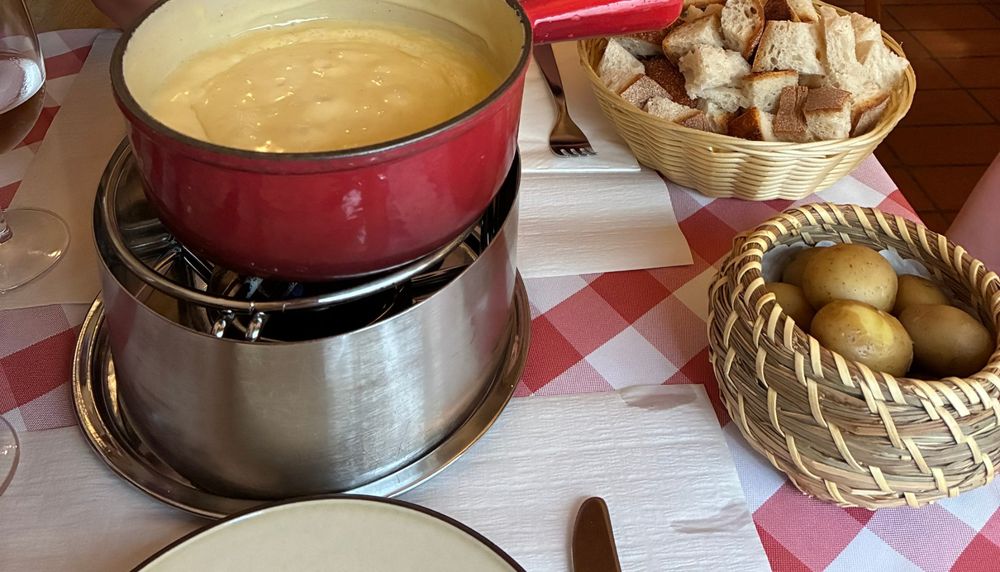A pot of cheese fondue with bread and potatoes on a checked tablecloth
